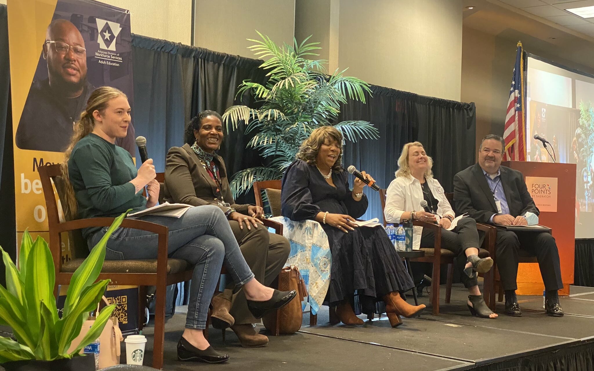 A panel of people sitting in chairs on a riser and interacting with an audience 