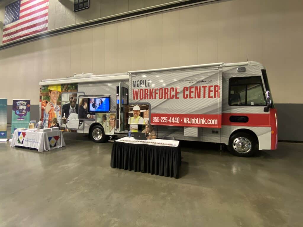 A large DWS mobile workforce center vehicle inside an enclosed arena with tables set up outside of it 