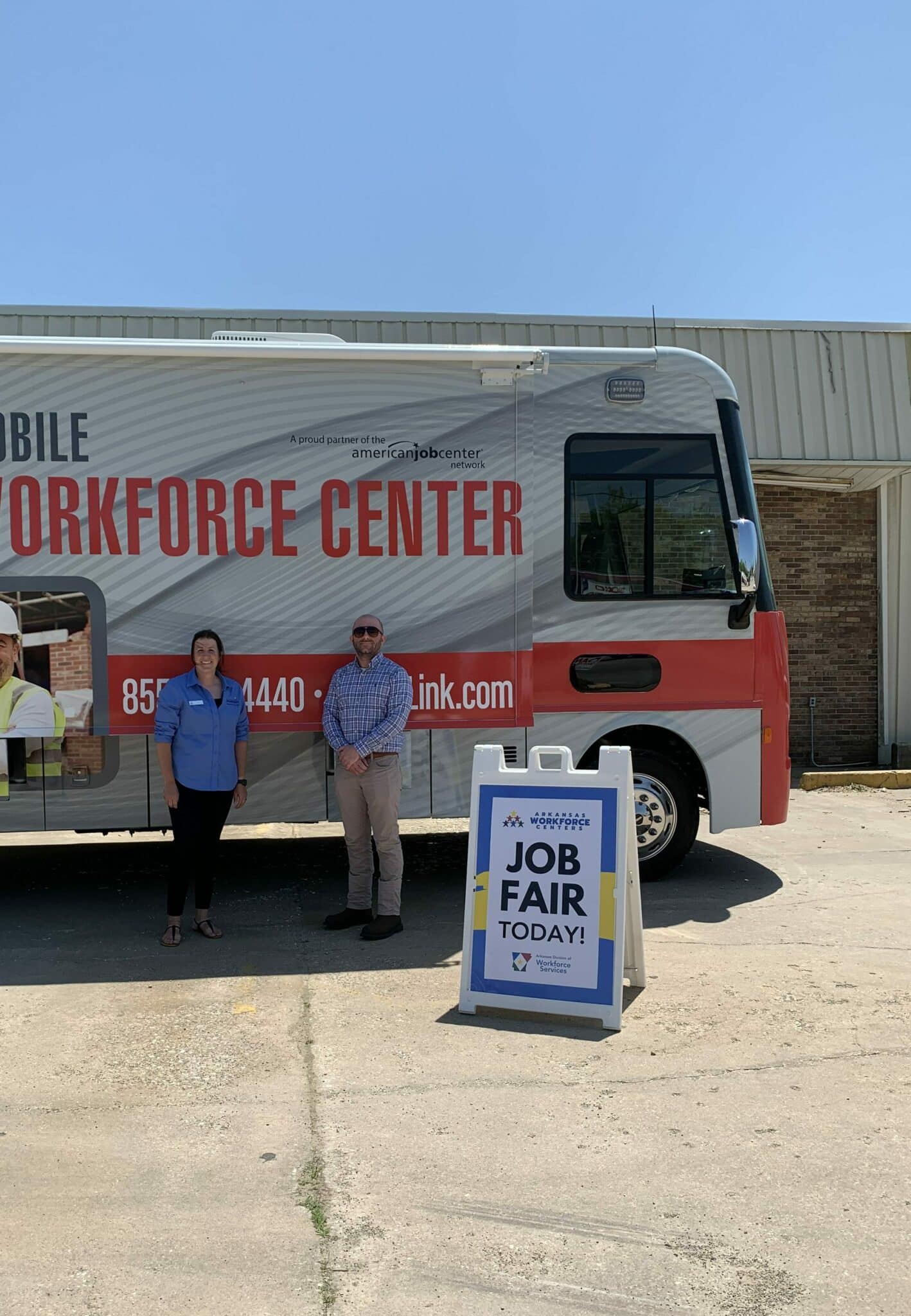 Two DWS employees posing along the side of a large mobile workforce center vehicle